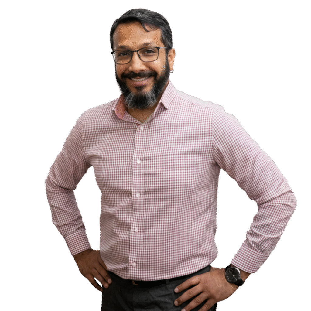 Adarsh (Adu) has a smile on his face as he stands with hans on hips. He's wearing glasses and is dressed in trousers and a shirt